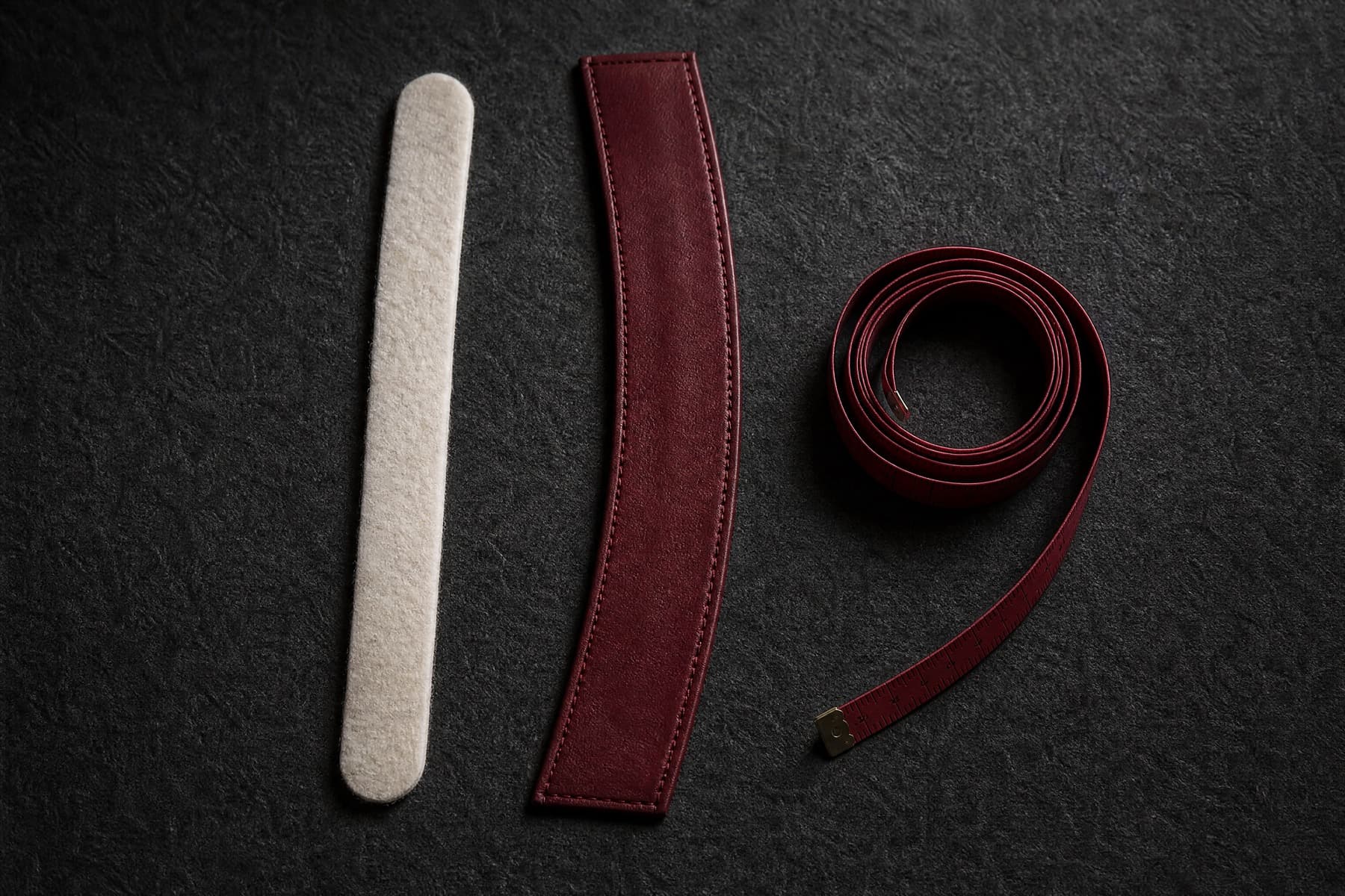 Bone felt sizing strip and wine leather sweatband laid flat beside a coiled measuring tape