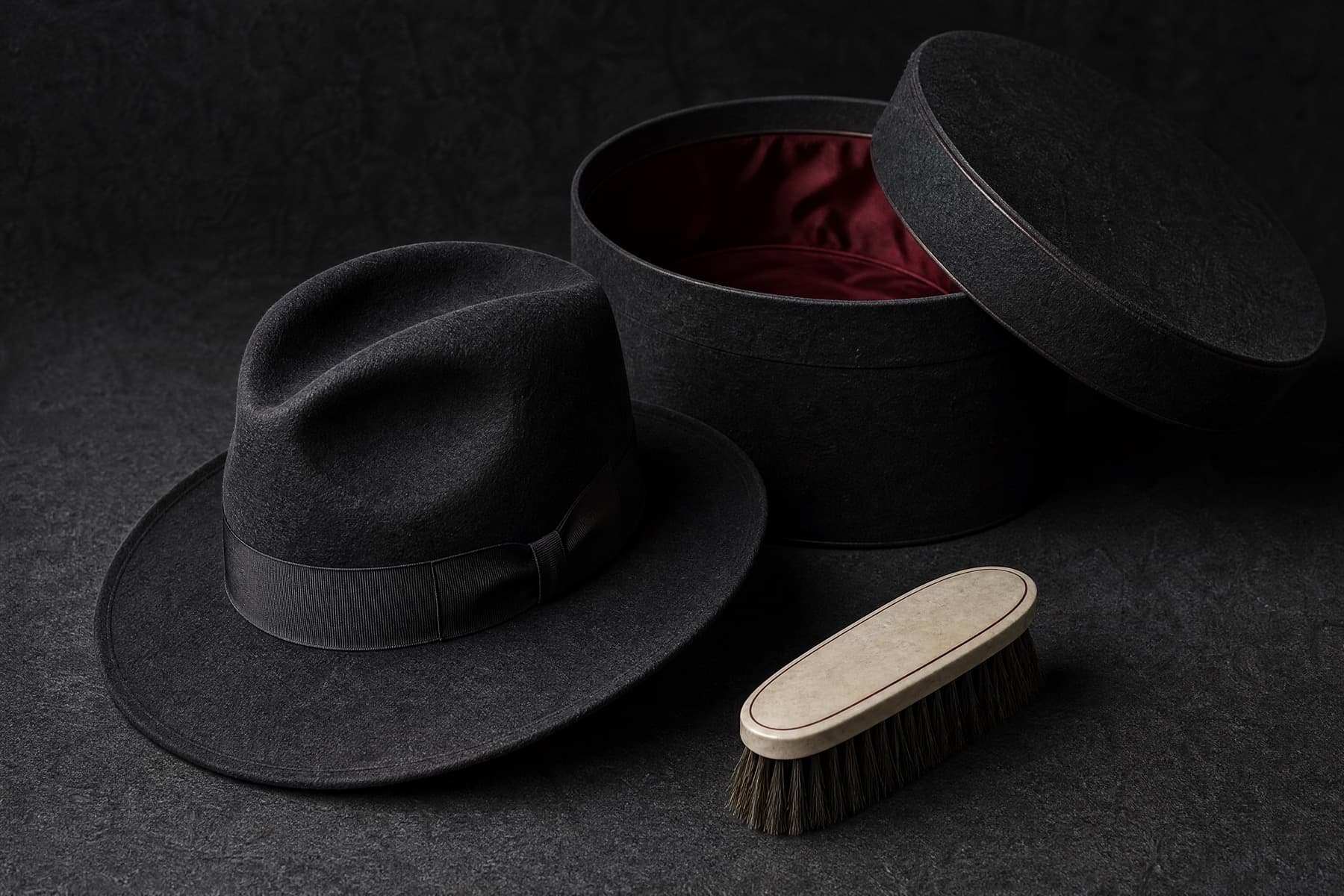 Rabbit felt fedora arranged with a rigid charcoal hat box and a bone-handled brush